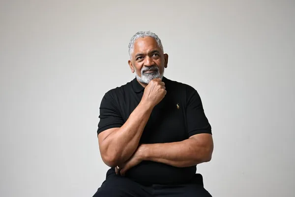 Chris Scott seated, hand to his chin, in a black polo shirt