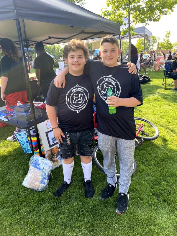 Two boys in Boys2Men shirts at an outdoor event.