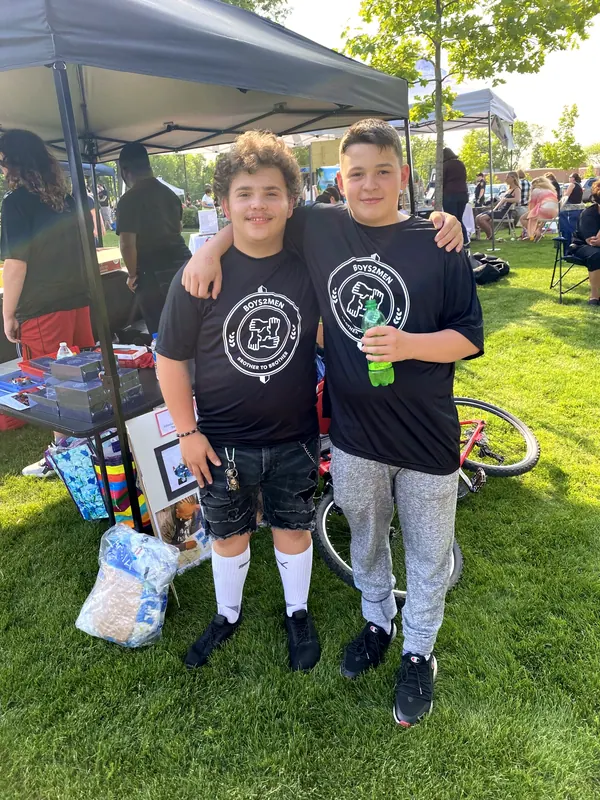 Two boys in Boys2Men shirts with their arms around each other.