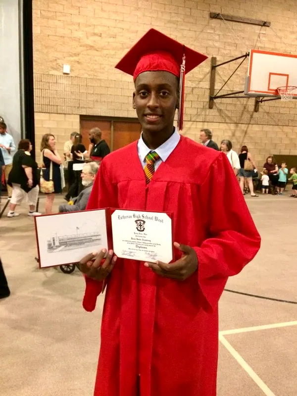 A young man in a red cap and gown holding his diploma.