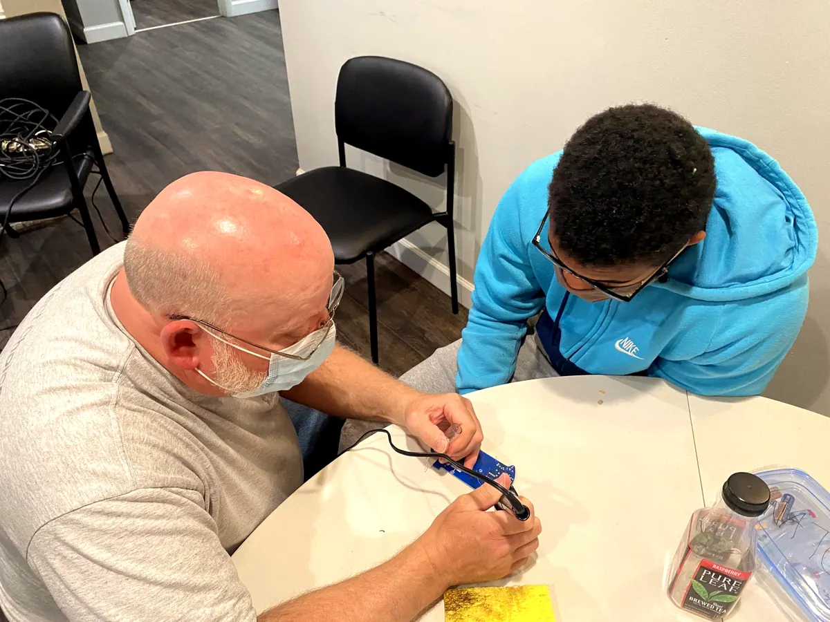 A Boys2Men mentor and a boy working on an electronics kit together at a table.