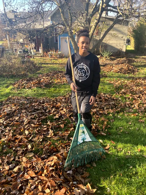 A boy with a rake in a yard full of leaves.