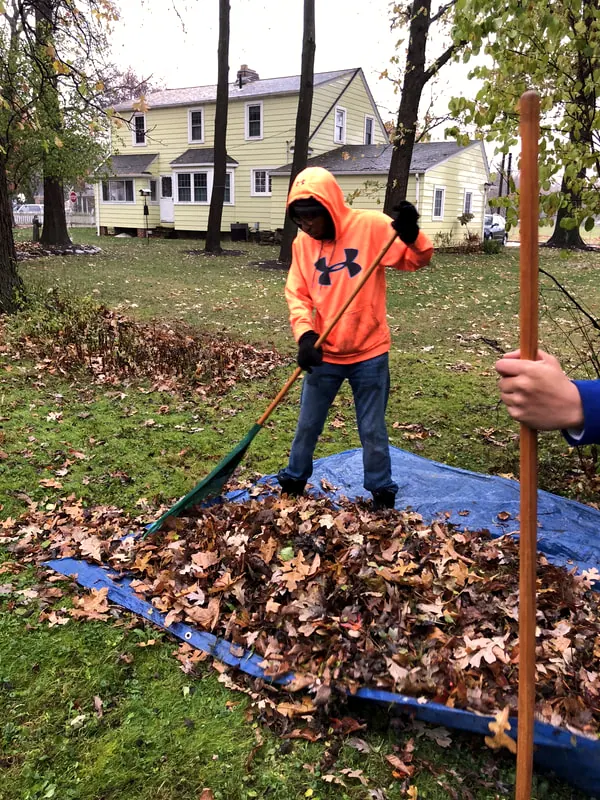 A boy raking leaves onto a tarp.