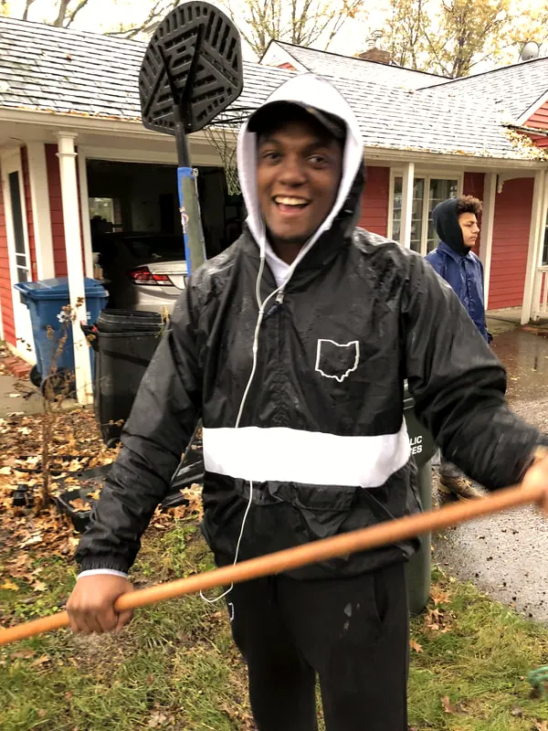 A boy laughing while raking leaves.