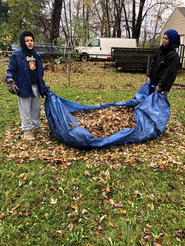 Boys hauling a tarp full of leaves.
