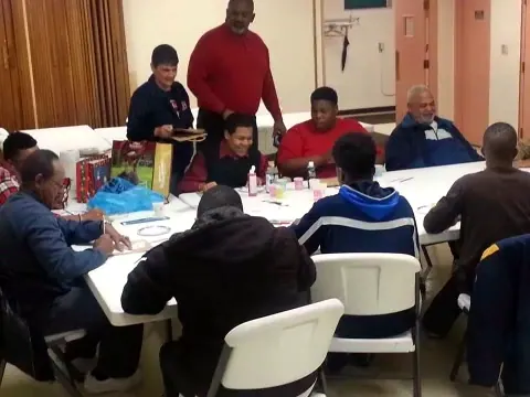 Boys and men gathered around tables in a hall.